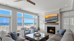 Un salón espacioso con chimenea, ventanas amplias con vistas a la playa y un ventilador de techo.