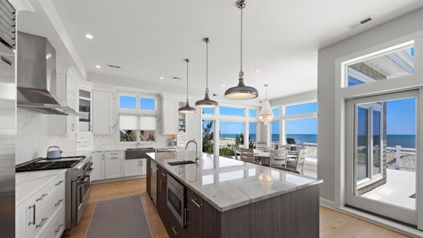 Una cocina moderna con una isla grande, armarios blancos, electrodomésticos de acero inoxidable e iluminación colgante.
