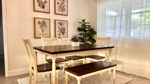 Un comedor con mesa y sillas de madera, impresiones botánicas enmarcadas en la pared y una planta en maceta.