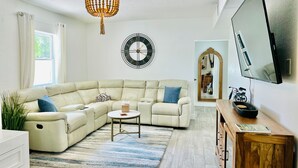 Una sala moderna con un sofá modular, un reloj redondo en la pared, un televisor y un mueble de madera.
