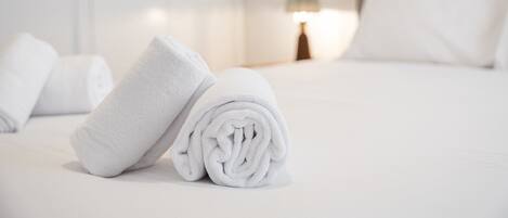A neatly made bed with white linens and a rolled towel on the side.