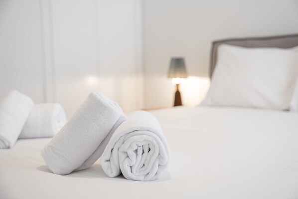 A neatly made bed with white linens and a rolled towel on the side.