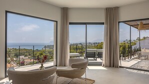 A modern room with large windows offering a view of the sea and greenery. There are two chairs and a table in the room. - Villa IKAL by Abahana Villas (Moraira)