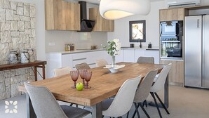 A modern kitchen with white cabinets, a wooden dining table, and a built-in oven. - Villa IKAL by Abahana Villas (Moraira)