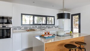 Uma cozinha moderna com armários brancos, uma ilha grande, um forno Bosch e uma janela com vista para um jardim.