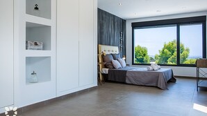 Quarto moderno com cama grande, estantes embutidas e vista para o verde através de amplas janelas.