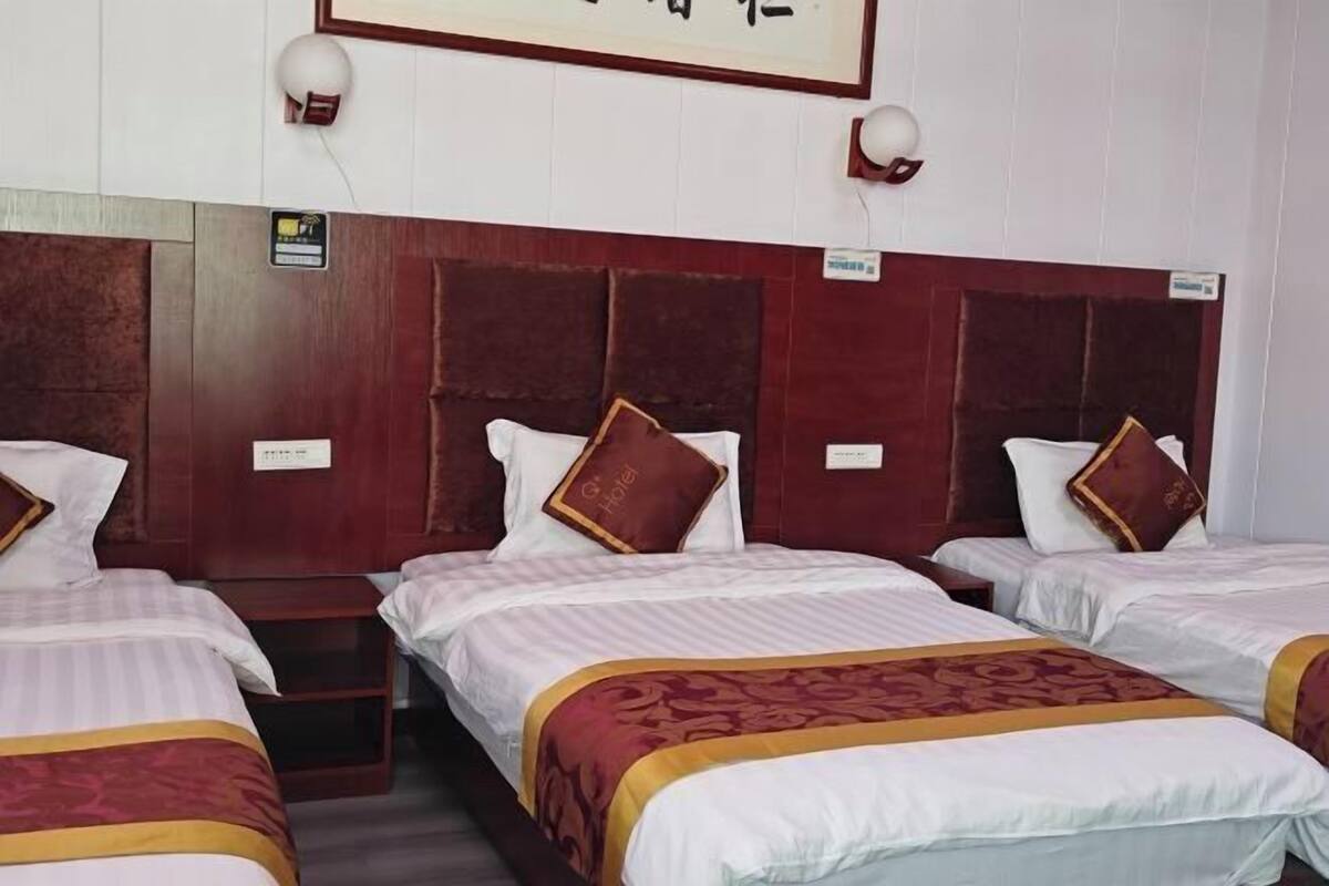 Una habitació d'hotel amb tres llits, cada un amb capçalera, taules de nit i un quadre encimbellat a sobre.