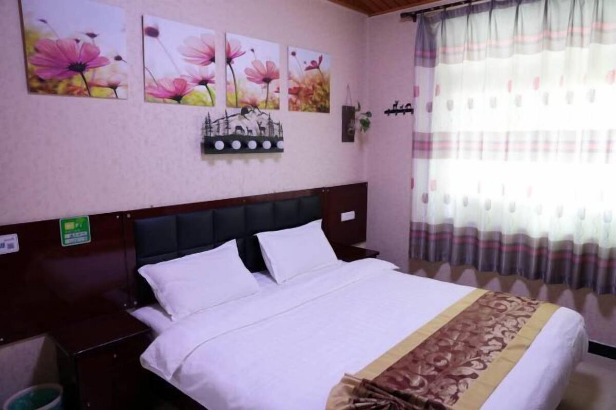 Habitació d'hotel amb llit, una tauleta de nit, prestatges fixats a la paret amb objectes decoratius i una finestra amb cortines.