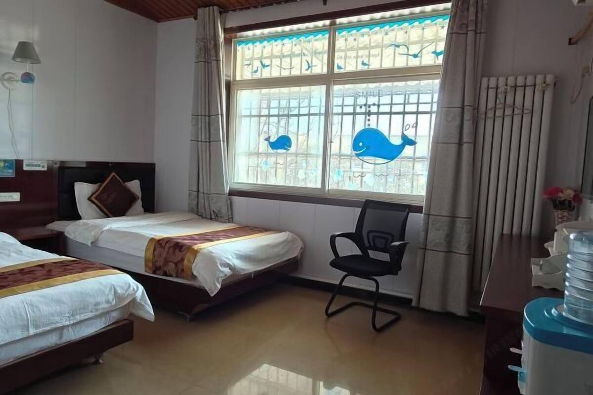 Una habitació d'hotel amb dos llits, una cadira, un escriptori, una finestra amb vista al mar i un dispensador d'aigua.