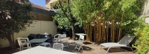En udendørs terrasse med træterrasse, hvide møbler og et bambushegn.