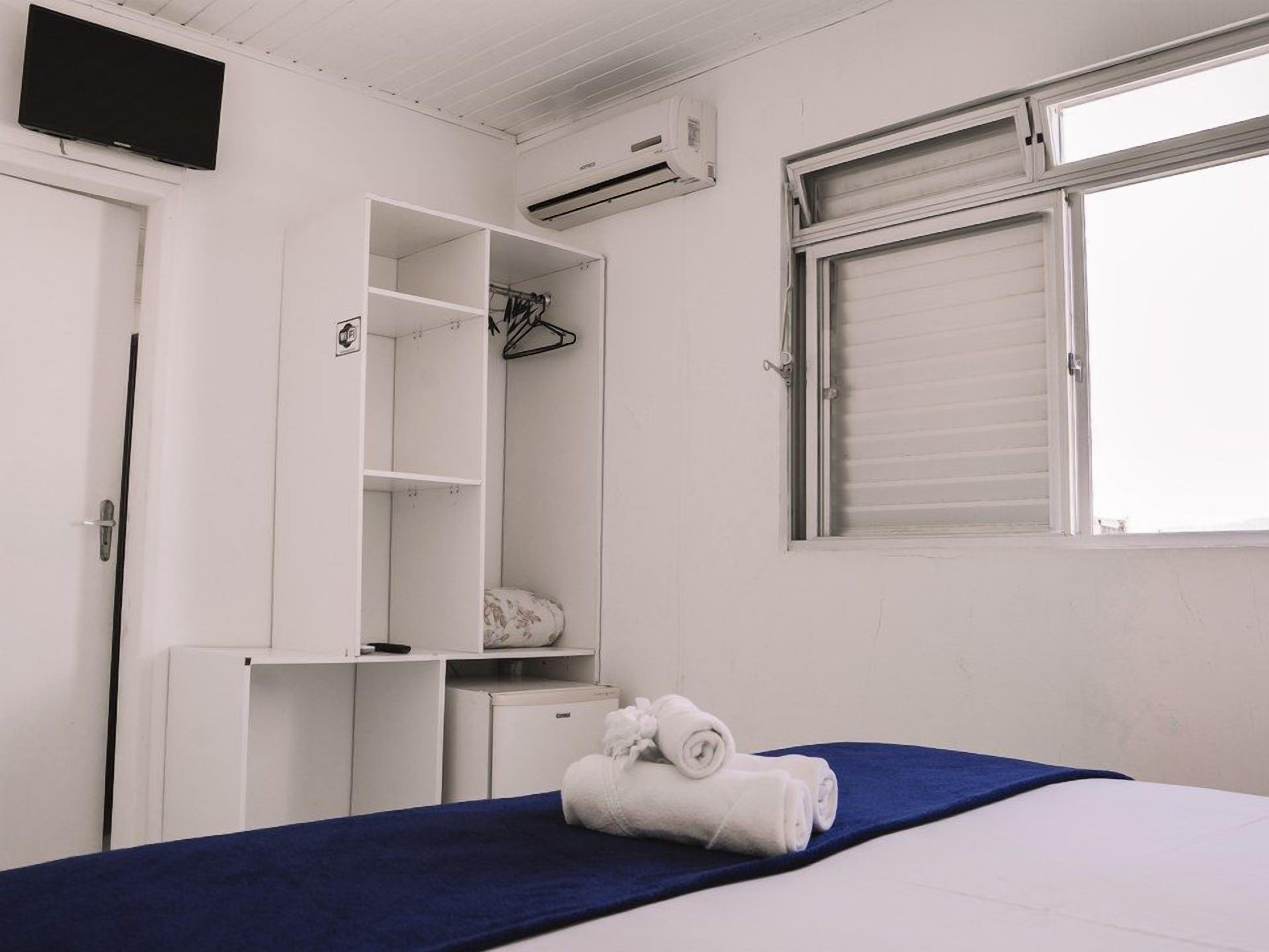 Un dormitorio con cama, armario, escritorio, aire acondicionado y ventana con persianas.
