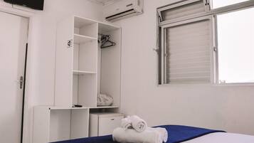 Un dormitorio con cama, armario, escritorio, aire acondicionado y ventana con persianas.