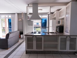 A modern kitchen with a central island, built-in cabinets, and a large window providing a view of the outdoors. - Hanna Amsterdam Hotel & Eventos (Florianópolis)