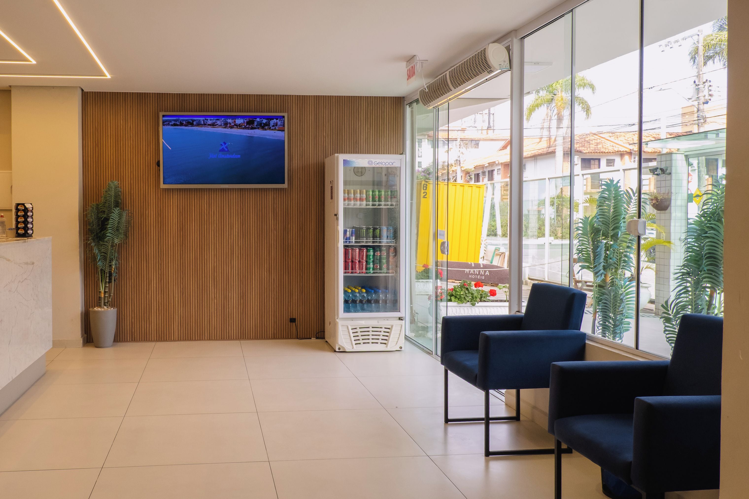 Zona de recepción con televisión de pantalla plana, máquina expendedora de bebidas y asientos junto a un gran ventanal.
