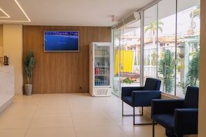 A reception area with a flat-screen TV, a beverage vending machine, and seating by a large window. - Hanna Amsterdam Hotel & Eventos (Florianópolis)
