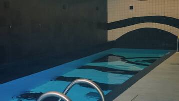 An indoor swimming pool with clear water, metal handrails, and tiled walls.