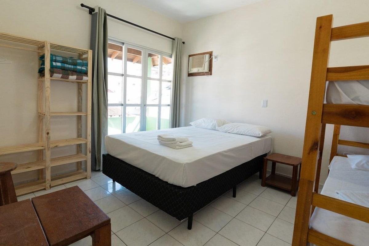 A bedroom with a bed, a wooden wardrobe, a small table, and a window with curtains.
