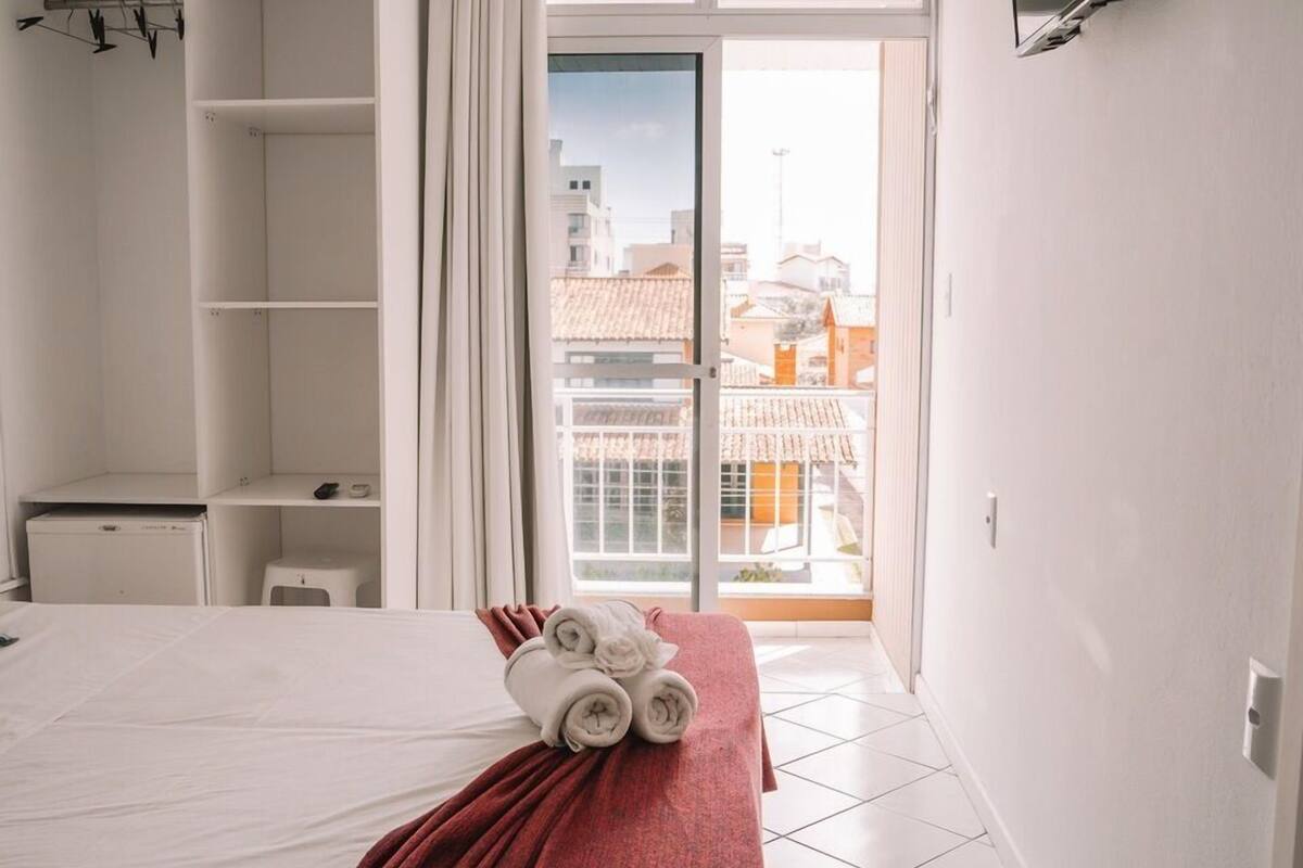 A hotel room with a bed, a red blanket, and a view of buildings through a glass door.