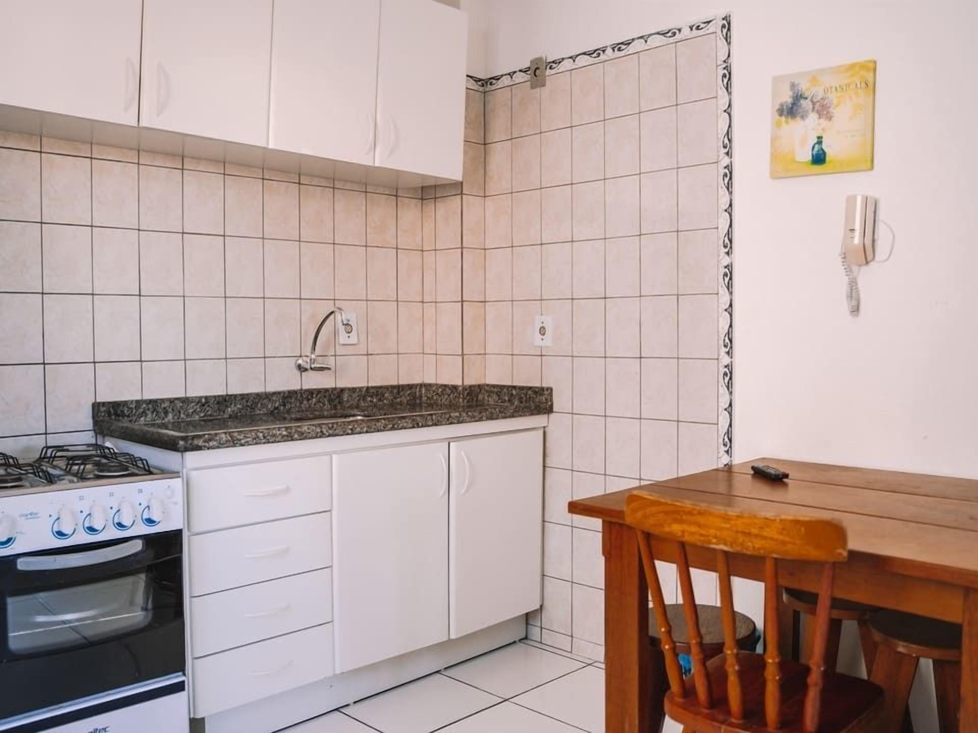 A kitchen with white cabinets, a gas stove, an oven, a granite countertop, and a wooden dining table with a chair.
