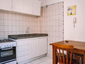 Cozinha com armários brancos, fogão a gás, forno, bancada de granito e mesa de jantar de madeira com uma cadeira.