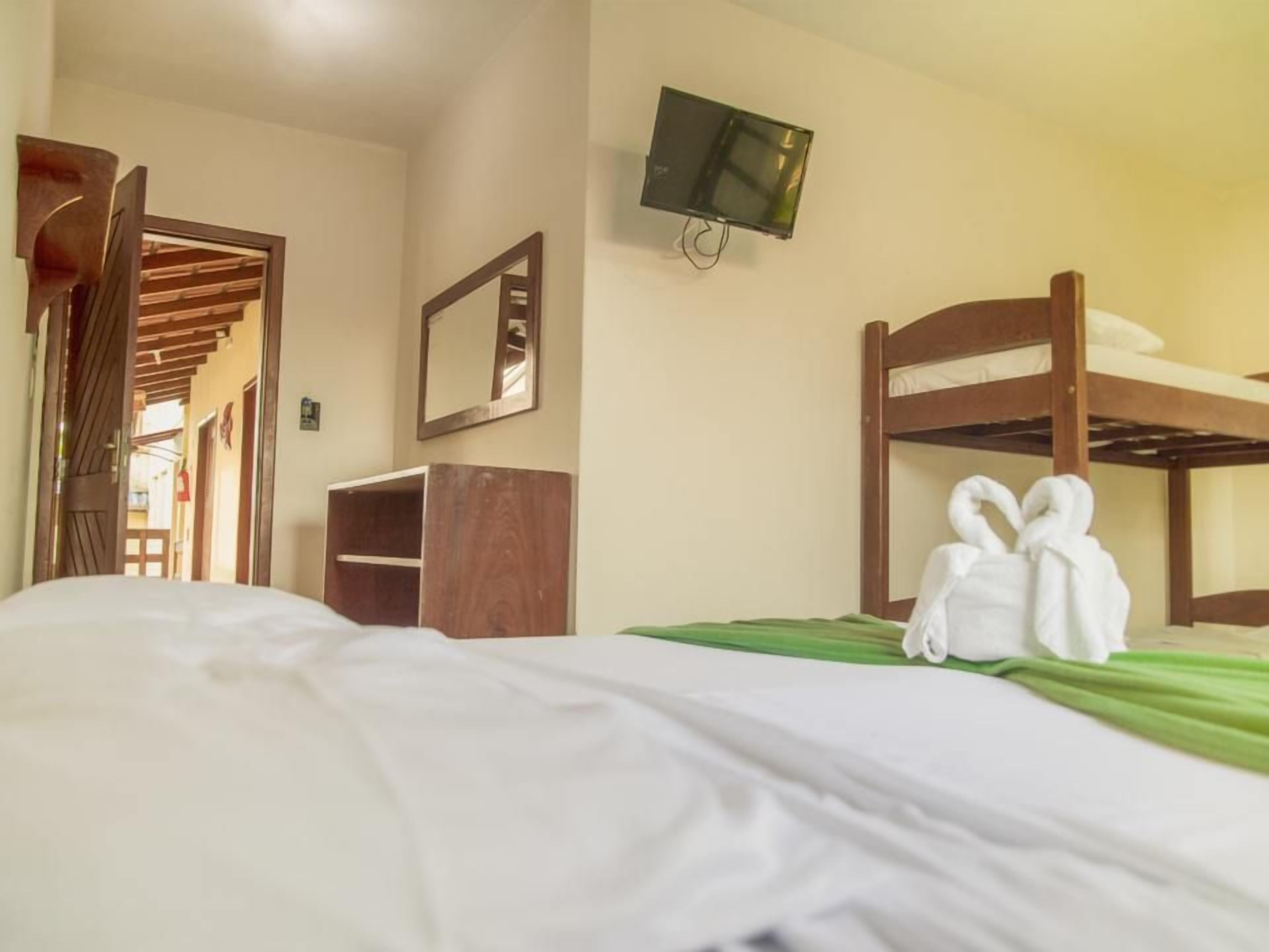 Una habitación de hotel con literas, un televisor montado en la pared, un armario de madera y un espejo.