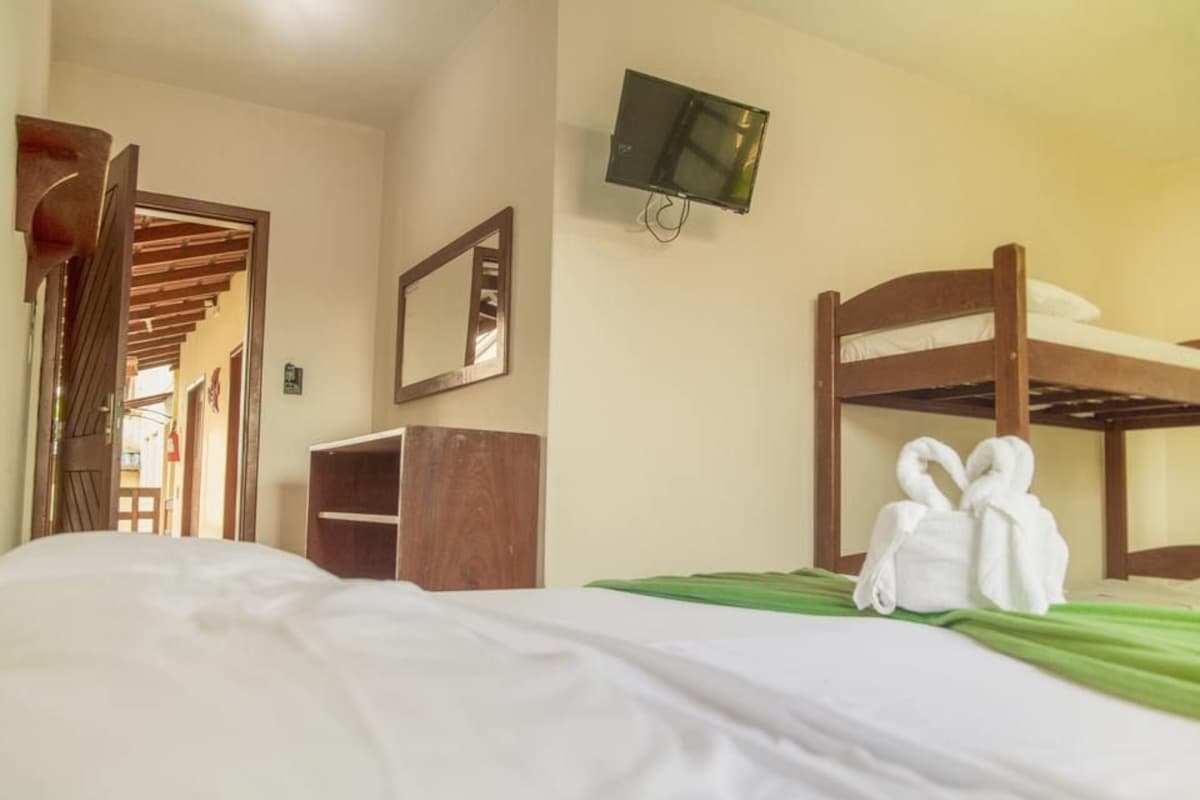 A hotel room with a bunk bed, a television mounted on the wall, a wooden wardrobe, and a mirror.