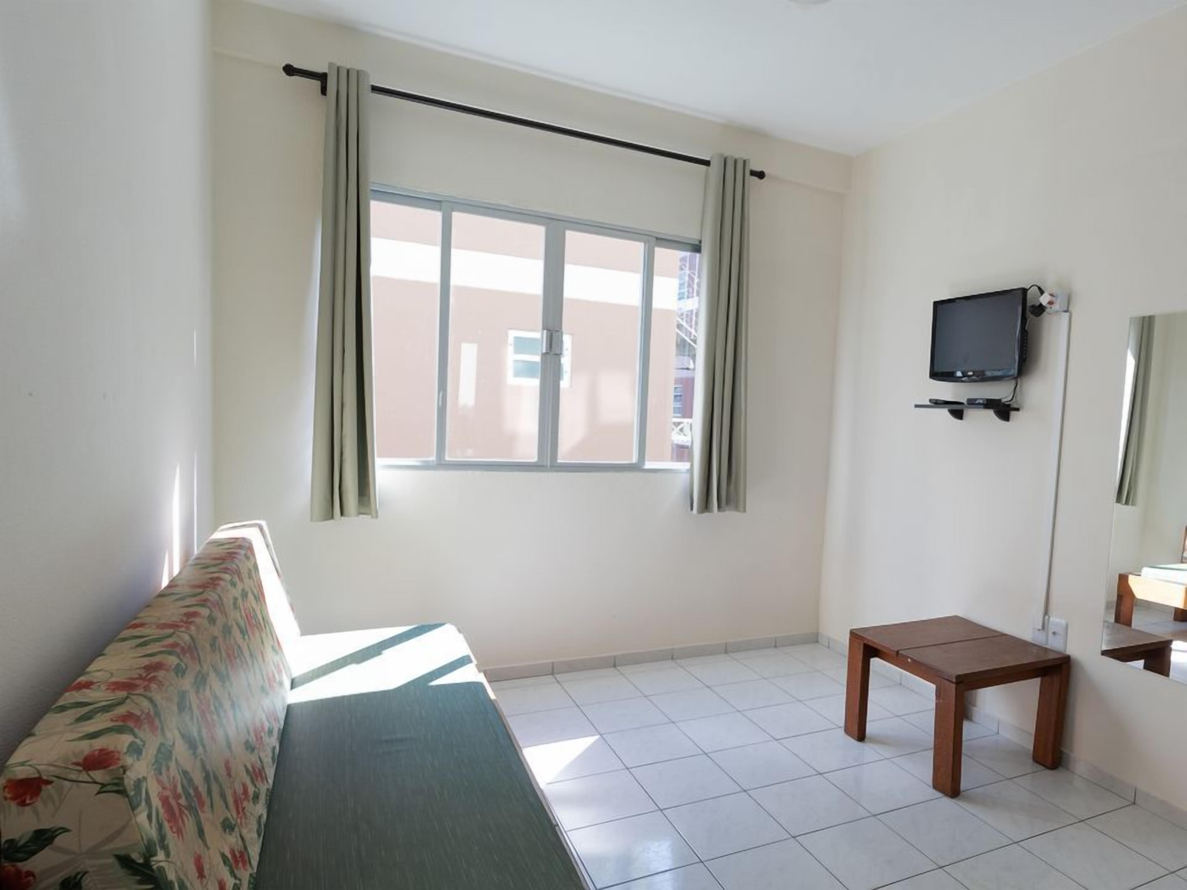 A room with a sofa, a small table, a television, and a window with curtains.