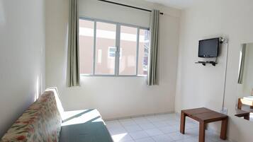 A room with a sofa, a small table, a television, and a window with curtains.