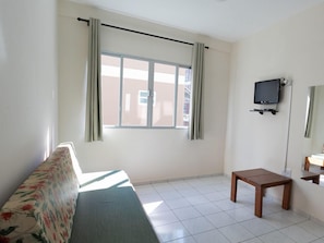 A room with a sofa, a small table, a television, and a window with curtains. - Hanna Amsterdam Hotel & Eventos (Florianópolis)