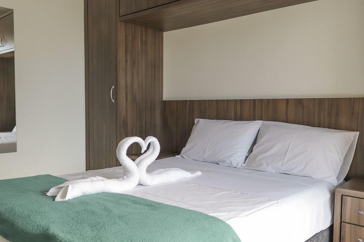 A hotel room with a bed, a green throw blanket, and a swan-shaped towel on the bed.