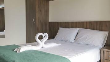 Habitación de hotel con una cama, una manta verde y una toalla con forma de cisne sobre la cama.