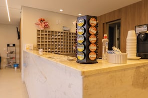A hotel reception area with a marble counter, a beverage dispenser, and a wall-mounted shelf with various items. - Hanna Amsterdam Hotel & Eventos (Florianópolis)