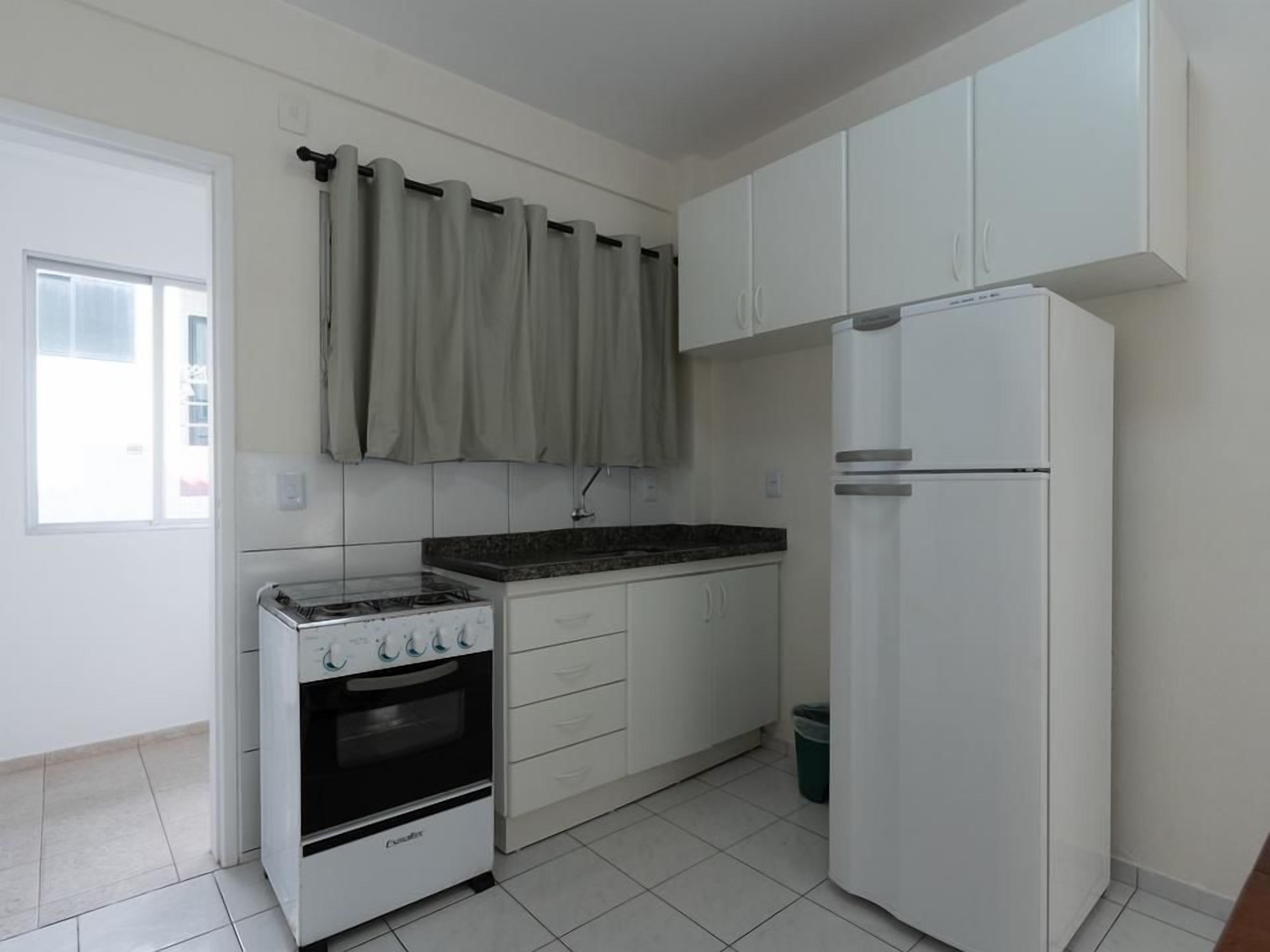 Una cocina con armarios blancos, un refrigerador blanco, una estufa y una ventana con cortinas.