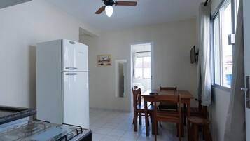 Una cocina con un refrigerador blanco, una estufa a gas, un ventilador de techo y un comedor con una mesa y sillas de madera.