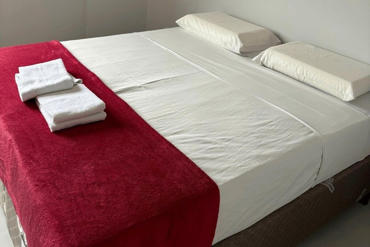 A single bed with white bedding, a red blanket, and two white towels on the side.