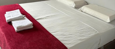 A single bed with white bedding, a red blanket, and two white towels on the side.