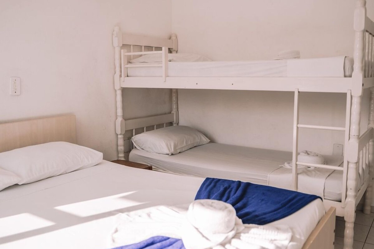 A dormitory-style room with bunk beds, a single bed, and a blue blanket on the lower bunk.
