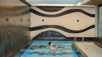 Una piscina interior con un diseño de azulejos ondulados en las paredes y una vista despejada del cielo.
