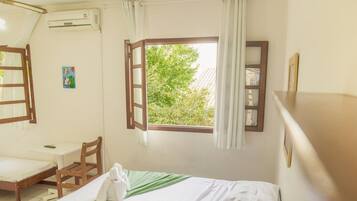 Una habitación con cama, escritorio y silla. Se ve un ventanal con cortinas, un equipo de aire acondicionado y un cuadro pequeño en la pared.