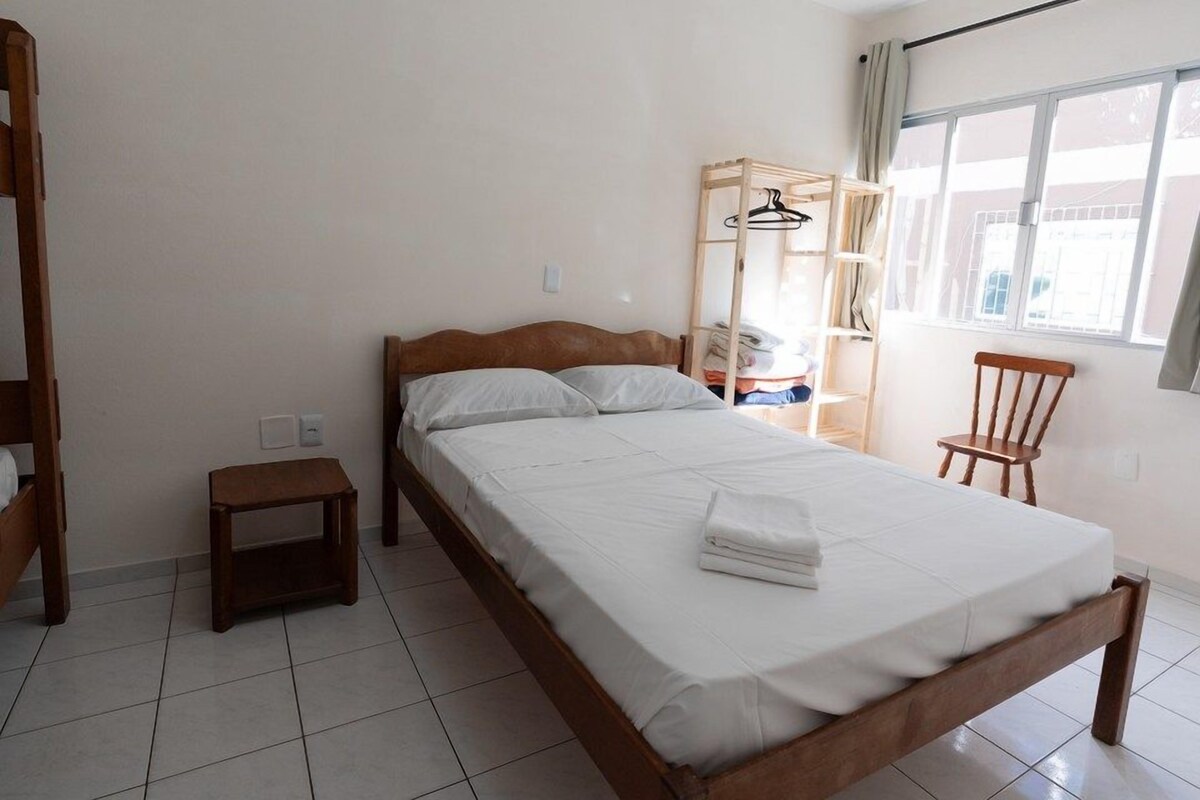 A bedroom with a wooden bed, a small bedside table, a wooden wardrobe, and a chair.