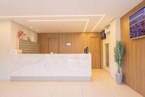 A reception area with a marble counter, wooden paneling, a potted plant, and a framed picture on the wall. - Hanna Amsterdam Hotel & Eventos (Florianópolis)