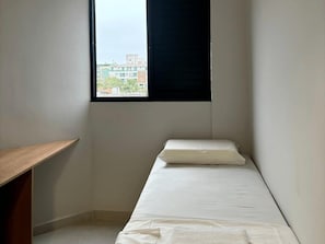 A small, single-bed room with a window, a wooden desk, and a view of buildings outside. - Hanna Amsterdam Hotel & Eventos (Florianópolis)