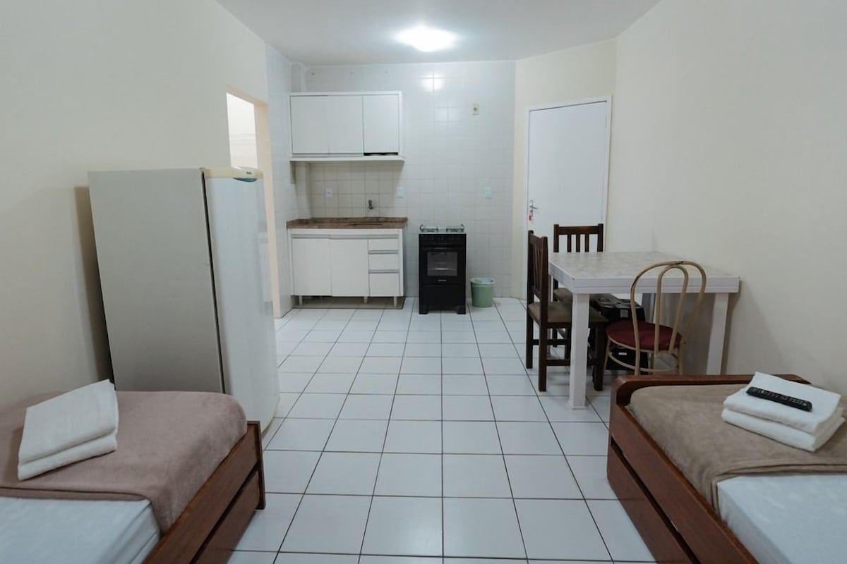 A compact room with two single beds, a small kitchenette, a dining table with chairs, and a white door.