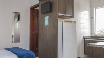 A hotel room with a bed, a small kitchenette, a TV mounted on the wall, and a window.