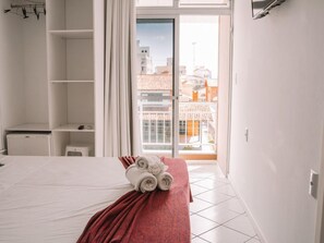 A hotel room with a bed, a red blanket, and a view of buildings through a glass door. - Hanna Amsterdam Hotel & Eventos (Florianópolis)