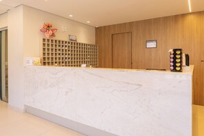 A reception desk with a marble top, a wooden panel wall, and a security camera. - Hanna Amsterdam Hotel & Eventos (Florianópolis)