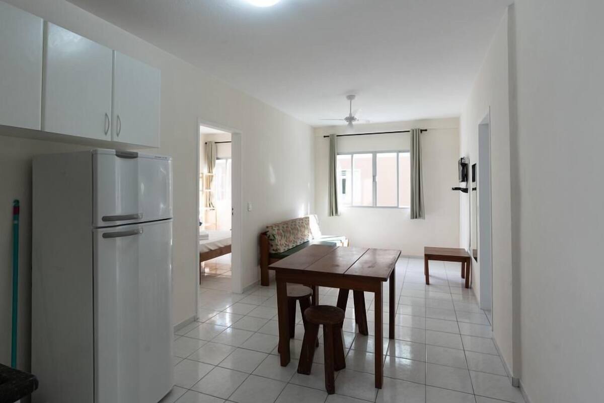 A compact kitchen with a refrigerator, a dining table with chairs, and a window with curtains.