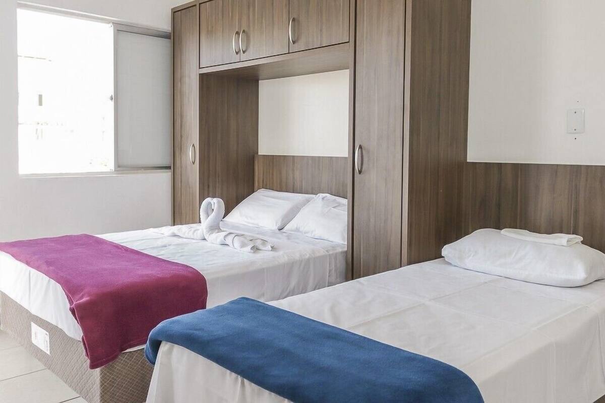 A hotel room with two single beds, a wardrobe, and a large window.