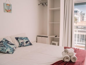 A hotel room with a bed, a wardrobe, a desk, and a window with a view of buildings. - Hanna Amsterdam Hotel & Eventos (Florianópolis)