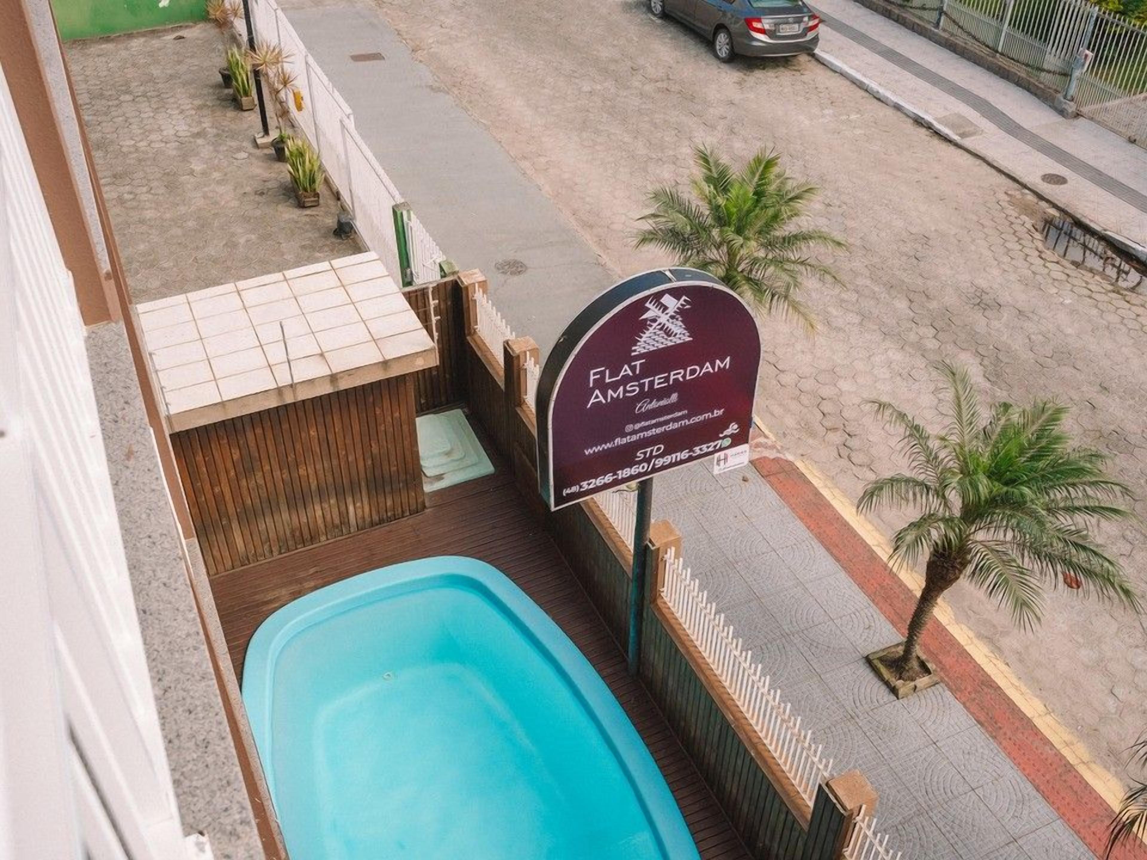 A sign for Flat Amsterdam, a swimming pool, and a street view with a parked car.